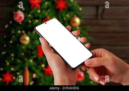 Weihnachts-Telefon-Mockup-Konzept. Smartphone in Frauenhand vor Weihnachtsbaum. Isolierte Anzeige für App-Werbung Stockfoto