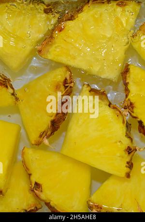 Nahaufnahme der gelben Ananasscheiben im Hintergrund der Limonade. Textur des kühlenden süßen Sommergetränks mit Makroblasen auf dem Weiß Stockfoto