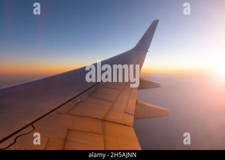 Flugzeug, das während des Sonnenuntergangs über dem Himmel fliegt. Flügel des Flugzeugs und Sonnenlicht Stockfoto