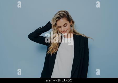 Schöne lächelnde Frau mit blonden gefärbten Haaren, die sich glücklich fühlen, während sie im Studio posiert Stockfoto