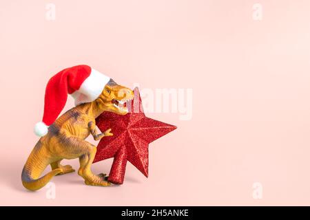 Dinosaurier Rex in rot Weihnachtsmann Hut hält Stern in den Pfoten auf rosa Hintergrund Silvester oder Heiligabend Art Weihnachtskarte Kreative Idee für Merry Stockfoto