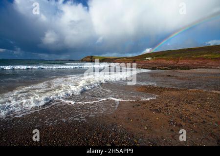 Manorbier Strand Pembrokeshire Wales Großbritannien mit Regenbogen endet bei weißen Hütte kopieren Raum Meer surfen Wellen kieselt guten Himmel Stockfoto