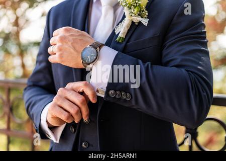 Bräutigam fixiert seine Manschettenknöpfe. Hübscher Bräutigam in dunkelblauem Anzug, der sich für die Hochzeit vorbereitet. Eleganter Bräutigam Hochzeitsmode. Stockfoto