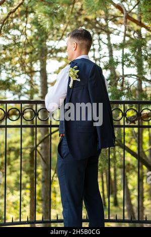 Hübscher junger Bräutigam mit elegantem dunkelblauem Anzug im Freien im Porträt. Modische Bräutigam-Mode. Rückansicht. Stockfoto