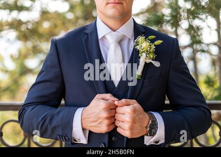 Unkenntlich junger Bräutigam im eleganten dunkelblauen Anzug mit schönen weißen Rosen boutonniere. Modische Details für den Bräutigam. Stockfoto