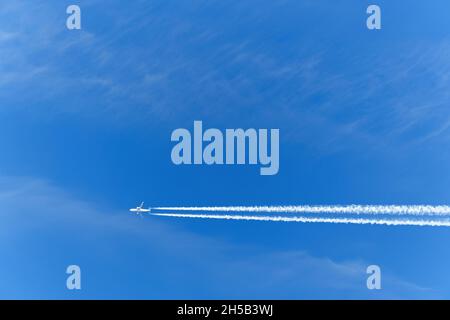 Ein Passagierflugzeug fliegt gegen einen blauen Himmel. Weiße Spur von den Turbinen des Flugzeugs. Hintergrund. Stockfoto