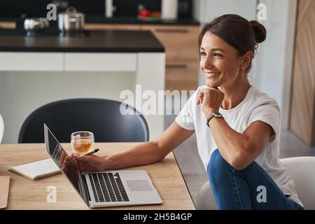Charmante kaukasische Geschäftsfrau, die online arbeitet, während sie zu Hause einen Laptop benutzt Stockfoto