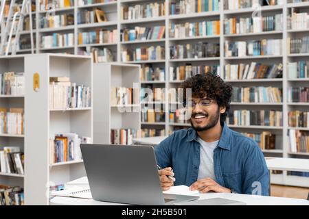 Männlicher Student, der in der Universitätsbibliothek mit einem Laptop studiert und Videoanruf führt Stockfoto