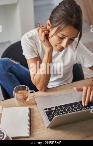 Schöne elegante hübsche Frau tippt Nachrichten auf Laptop in modernen Wohnungen Stockfoto