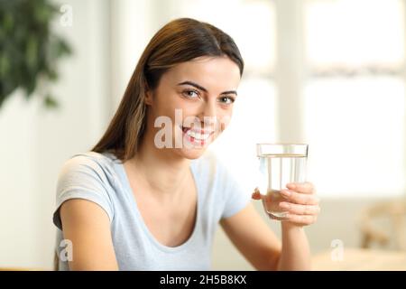 Glückliche Frau schaut Sie mit Wasserglas zu Hause an Stockfoto