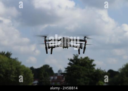 Eine DJI Mavic 2 Pro Drohne schwingt tagsüber in der Luft, mit blauem Himmel und einer hellen Wolkenkulisse. Die Drohne wird im Flug über einem belaubten A gefangen genommen Stockfoto