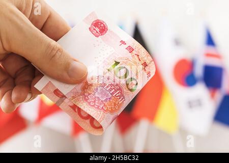 100 Yuan in der Hand vor dem Hintergrund von Flaggen verschiedener Länder, Nahaufnahme Stockfoto