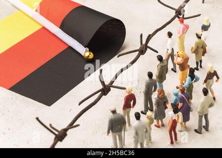 Plastikspielzeugmänner, Stacheldraht und deutschlandflagge, das Konzept von Migranten, die die Grenze überqueren Stockfoto