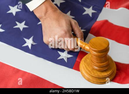 Die Hand des Richters hält einen Holzgavel, um auf einen klingenden Block im Gerichtssaal auf der Flagge der vereinigten staaten von amerika zu knallen. Stockfoto