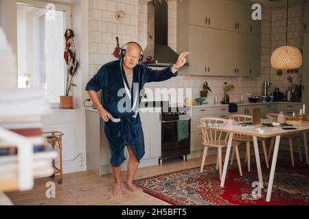 Älterer Mann tanzt, während er Musik über Kopfhörer in der Küche genießt Stockfoto