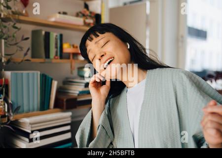 Junge Frau, die zu Hause über kabellose in-Ear-Kopfhörer Musik hört Stockfoto