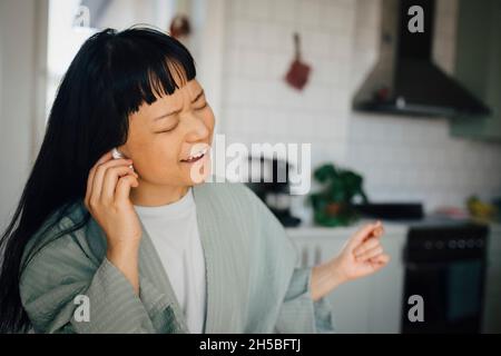 Fröhliche junge Frau, die zu Hause Musik hört und singt Stockfoto