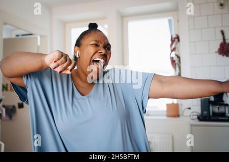 Fröhliche Frau, die zu Hause in der Küche Musik hört Stockfoto