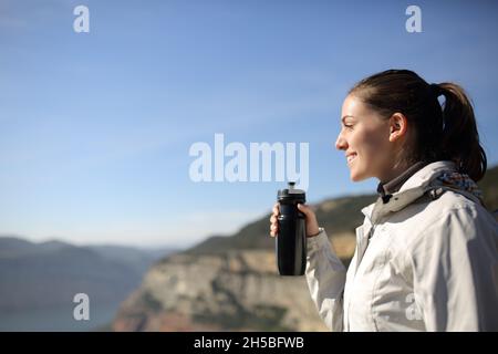Seitenansicht Porträt eines glücklichen Trekkers, der eine Wasserflasche hält und wegschaut Stockfoto