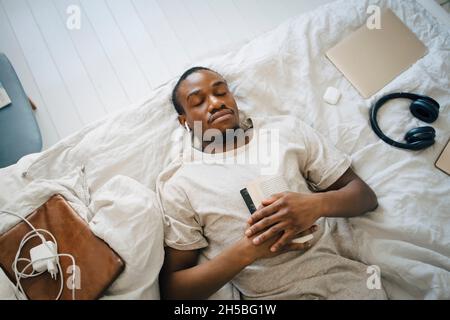 Direkt über dem Blick auf den Mann, der mit Buch auf dem Bett zu Hause schläft Stockfoto