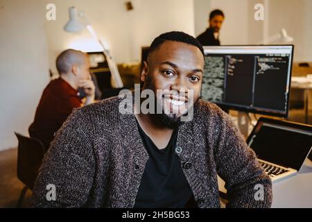 Porträt eines jungen männlichen Programmierers von einem Kollegen, der am Schreibtisch in einem Startup-Unternehmen arbeitet Stockfoto