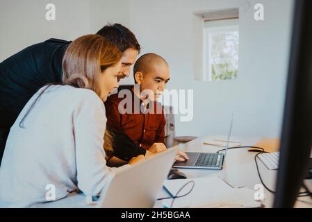 Weibliche und männliche Hacker konzentrieren sich beim Codieren über Laptops im Kreativbüro Stockfoto