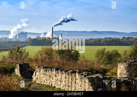 Wände einer alten Ruine aus Naturstein mit einer Fabrik mit rauchenden Kaminen im Hintergrund vor der Gebirgslinie am Horizont Stockfoto