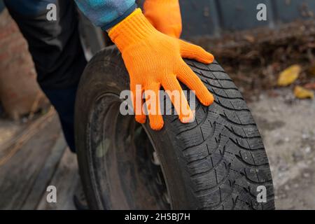 Winterreifen austauschen. Kfz-Mechaniker Hände in Sicherheitshandschuhe halten Winterreifen. Auto Vorbereitung für die Wintersaison Konzept Stockfoto