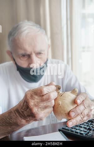 Die Hände des alten Mannes legten Geldmünzen in eine Sparschwein, das Konzept der Rente, Ersparnisse, Inflation, Alter. Stockfoto