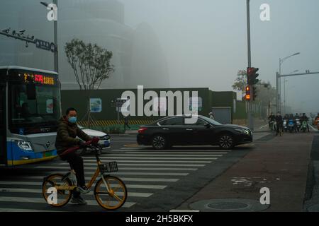 Ein Mann fährt mit dem Fahrrad an Hochhäusern in Pekings zentralem Geschäftsviertel vorbei, die von starkem Smog in Peking, China, umhüllt sind. 06-Nov-2021 Stockfoto