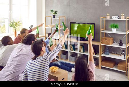 Eine Gruppe von Freundinnen und Männern, die vor dem Fernseher sitzen und ein Fußballspiel emotional beobachten. Stockfoto