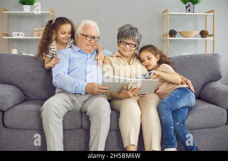 Glückliche Großeltern und ihre beiden Enkelinnen schauen sich zusammen ein Fotobuch mit einem Familienfoto an. Stockfoto