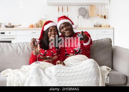 Glückliches schwarzes Paar, das Fernsehen schaut und zu Hause Champagner trinkt Stockfoto