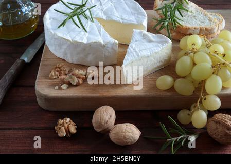 Köstlicher Brie-Käse mit Nüssen, Trauben und Wein auf einem Holzschneidbrett. Camembert-Käse. Stockfoto
