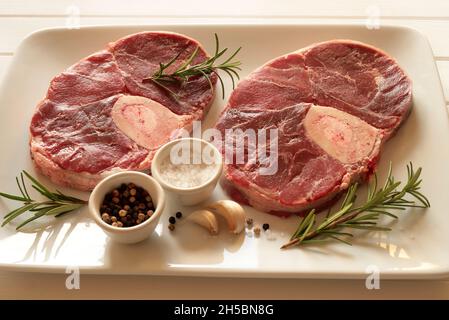 Roher frischer Ossobuco con mit Kräutern auf weißem Hintergrund. Geschmortes Kalbsfleisch. Direkt darüber. Stockfoto