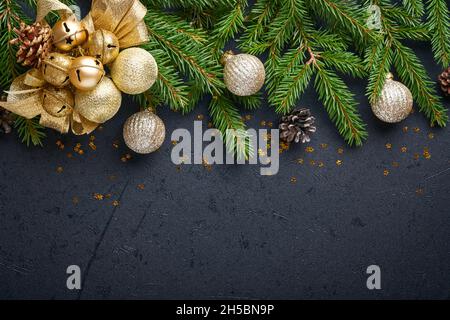 Weihnachtsdekoration. Weihnachtsdekorationen mit goldenen Kugeln, Zapfen, Glocken, Tannenzweigen und präsentieren auf dunkelschwarzem Hintergrund. Bordüre. Draufsicht. Stockfoto