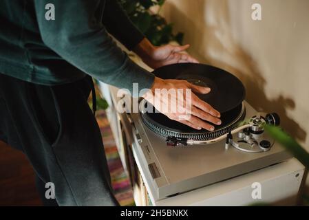 Junger Tausendjähriger Hipster mit gemischtem Rennen, der sich in der Wohnung entspannt und Vinyl-Schallplatten hört. Vinyl-Schallplatten spielen, junge Hände Platten drehen Stockfoto