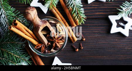 Mischung aus Glühweingewürzen in einem Glas Anis, Kardamom, Piment, Zimtstangen, Nelken auf dunklem Holzgrund. Für Text platzieren. Stockfoto