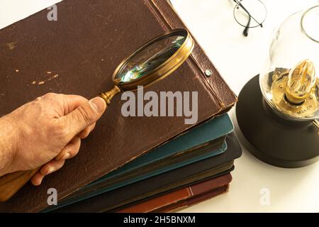 Hand hält eine Lupe über alten Fotoalben, Leuchtende Vintage-Lampe, Konzept der Erinnerungen und historische und familiäre Forschung Stockfoto