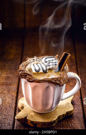 Vegane heiße Schokolade im weißen rustikalen Becher, Holzhintergrund und Rauch, heißer Winterdrink Stockfoto
