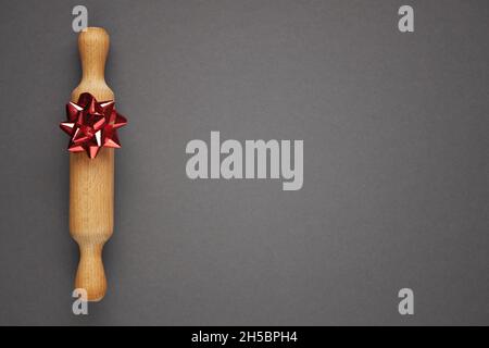 Holz-Nudelholz mit roter Schleife auf grauem Hintergrund. Konzept für festliches Backen. Speicherplatz kopieren. Stockfoto