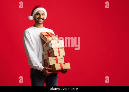 Frohe Weihnachten. Glücklicher Arabischer Mann In Santa Hat Hält Viele Geschenkboxen Stockfoto