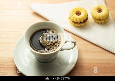 Eine Tasse Kaffee mit zwei butterhaltigen Keksen, die mit Zucker auf einer Holzoberfläche bestreut wurden. Stockfoto