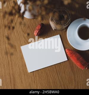 Herbst Herbst Stillleben. Papierkarte Mockup, Tasse Kaffee, Herbstdekoration, Vase mit getrockneten Blumen auf Holztisch. Stockfoto