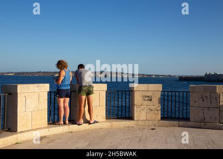 Sizilien, Siracusa, Ortigia - 20. Juli 2021: Menschen, die das Meer auf der Promenade von Ortigia betrachten Stockfoto