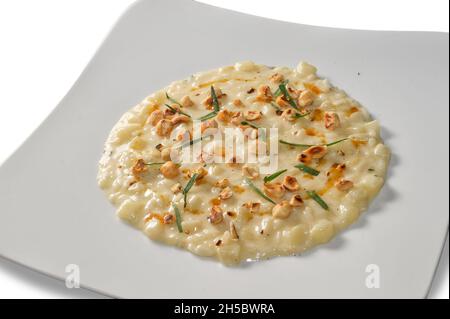 Risotto mit Robiola di Roccaverano Käse mit runden und sanften Haselnüssen aus der Langhe auf weißem Teller auf weißem Grund Stockfoto