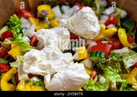 Makro-Nahaufnahme von frischem Salat mit gelben Paprika, Tomaten und Burrata Mozzarella italienischen Käse zerkleinert cremig innen Stockfoto
