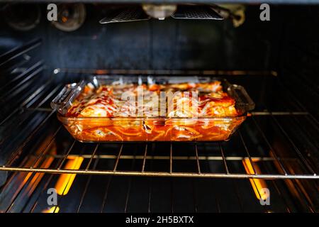 Innenofen mit Gestell und hausgemachten mexikanischen Speisen Enchiladas in Backblech Glas Gericht Kochen mit Tomatensauce, Tortilla und Käse Stockfoto