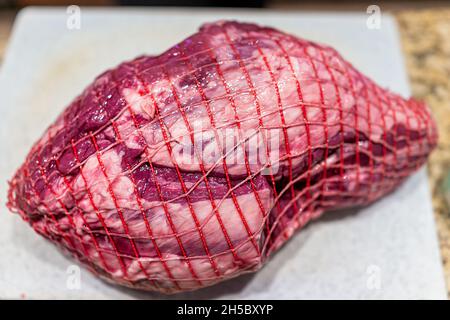 Rotes rohes neuseeländisches oder australisches Lammfleisch mit Ganzbeinstück mit Gitterverpackung auf Schneidebrett für die Zubereitung des Kochens Stockfoto