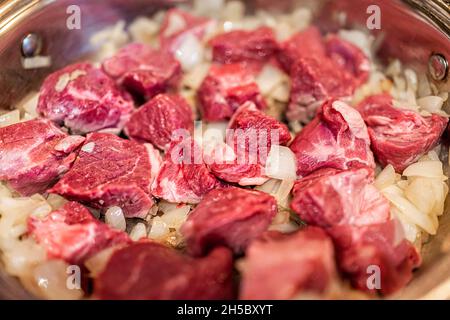 Rote, rohe Lamm- oder Rindfleischschulterkoteletts, die in einer Pfanne über Zwiebeln geschnitten werden, um traditionelle kasachische oder usbekische Pilaf oder Plov-Makro-Nahaufnahme zu machen Stockfoto